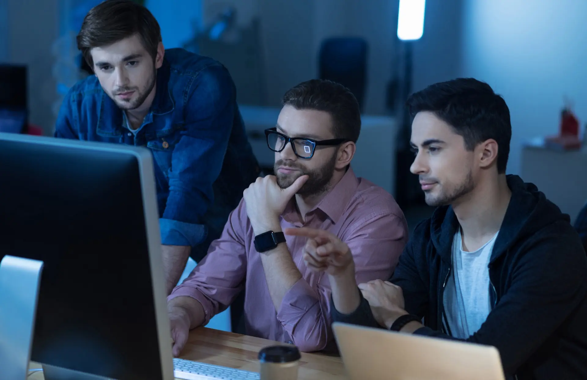 man sitting with his colleagues in front of the computer and pointing at it while working together