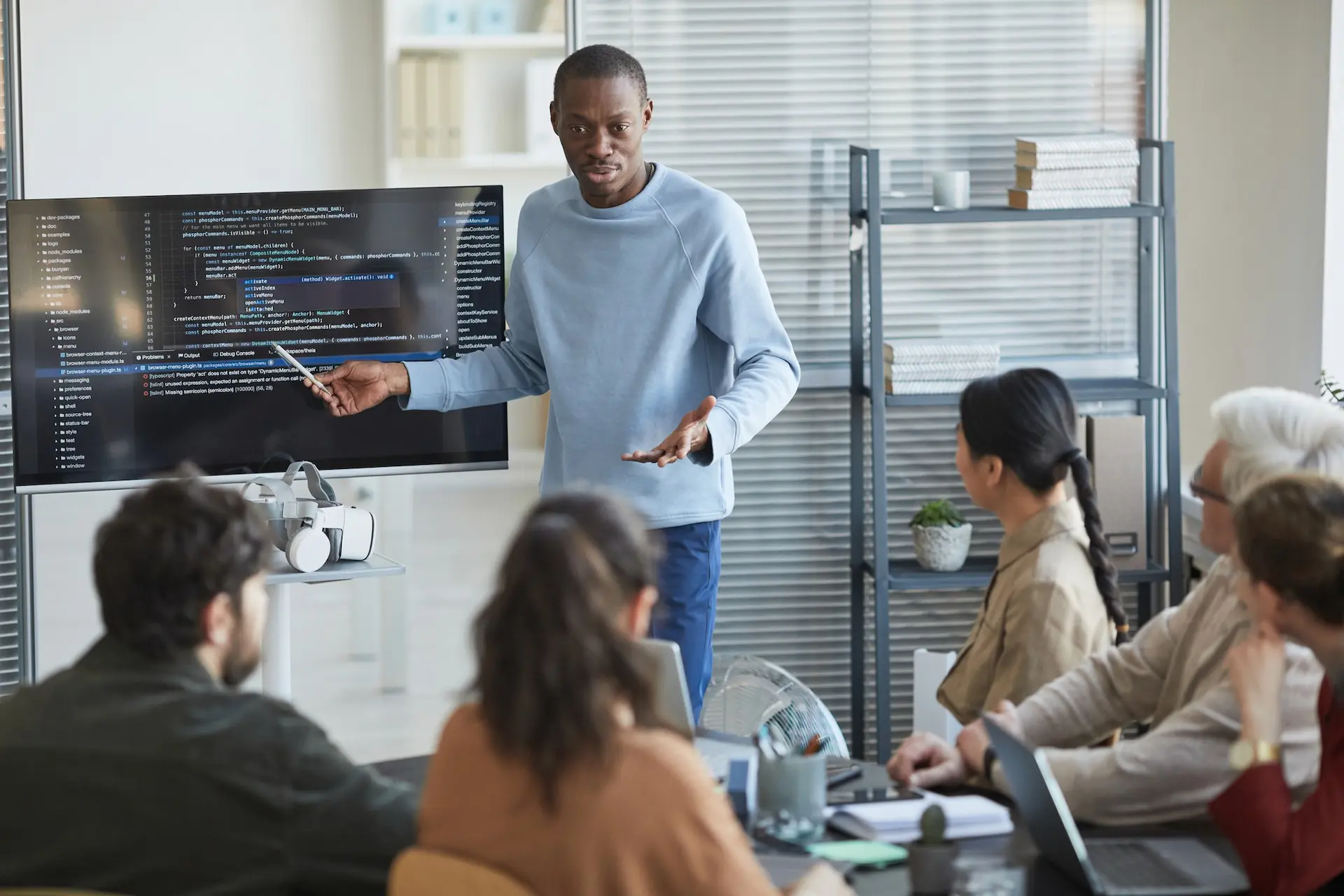 Man giving presentation in office to it team and pointing at code on screen.